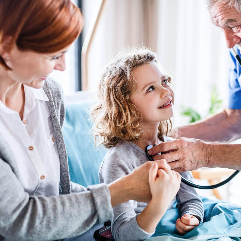 Young-girl-sitting-on-her-mother’s-lap-during-a-doctor’s-consultation-smiling