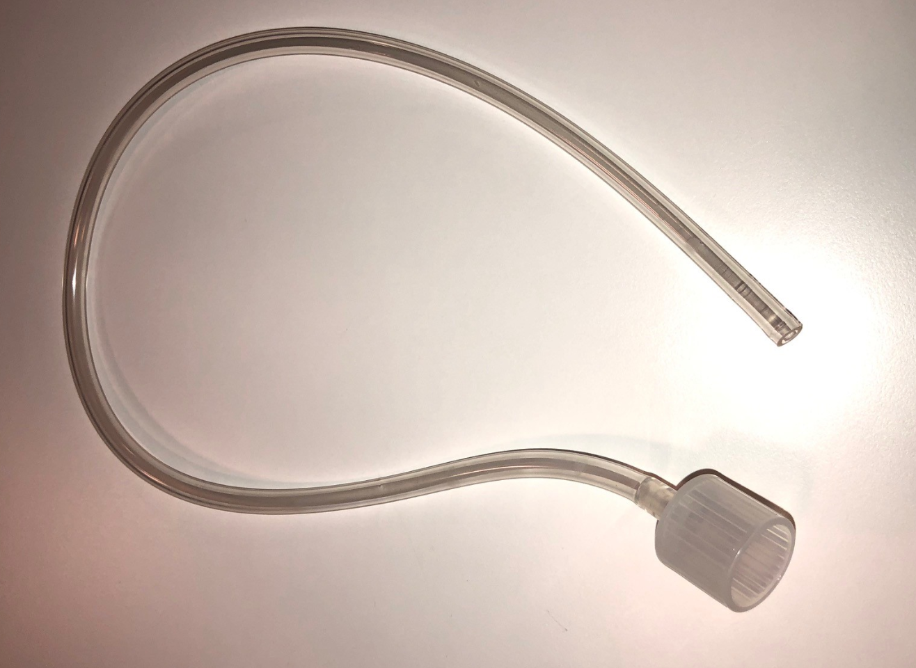 A clear plastic tube with a ridged cap on one end, coiled on a white surface.