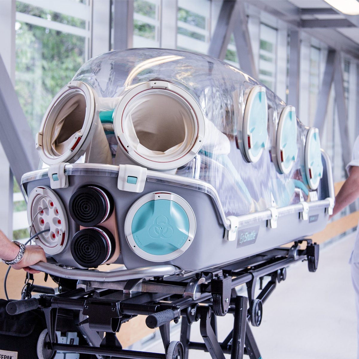 Medical isolation transport stretcher with transparent cover and arm ports on a hospital corridor.