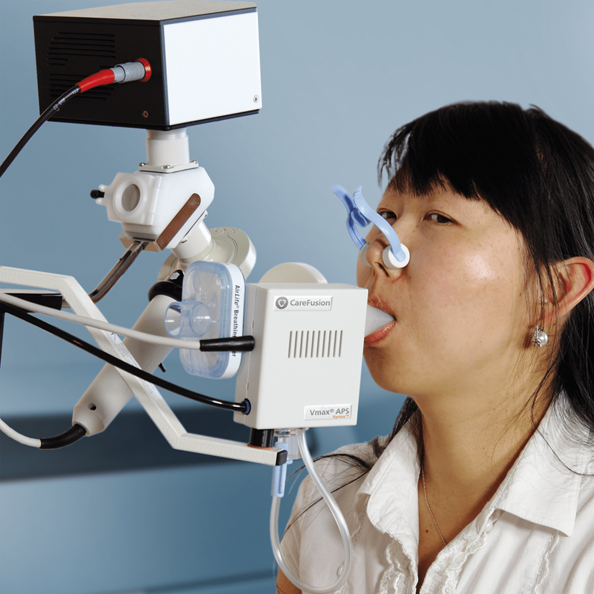 Woman undergoing a lung function test with a spirometry device and nose clip in a medical setting.