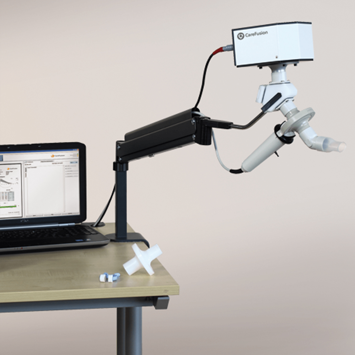 Laptop and a spirometer with a CareFusion device arm on a wooden desk, medical accessories beside.