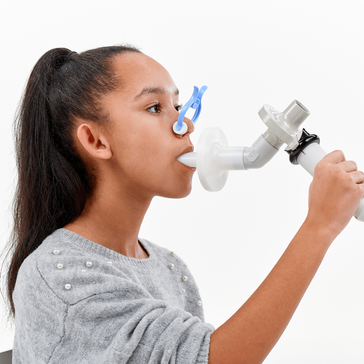 Girl with ponytail doing a lung function test with nose clip and mouthpiece, wearing a grey sweater.