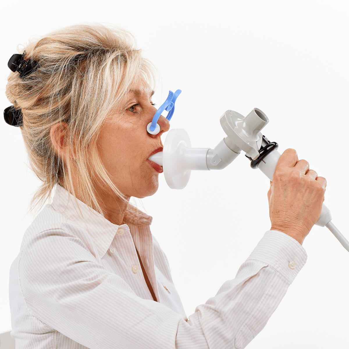 Woman using a spirometer with a mouthpiece and nose clip for a pulmonary function test.