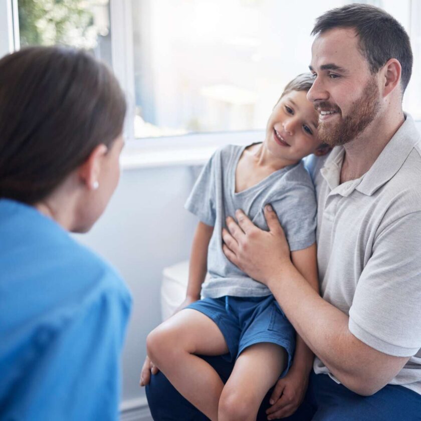 Doctor-consulting-a-young-boy-who-is-sitting-on-his-father’s-lap-in-a-hospital