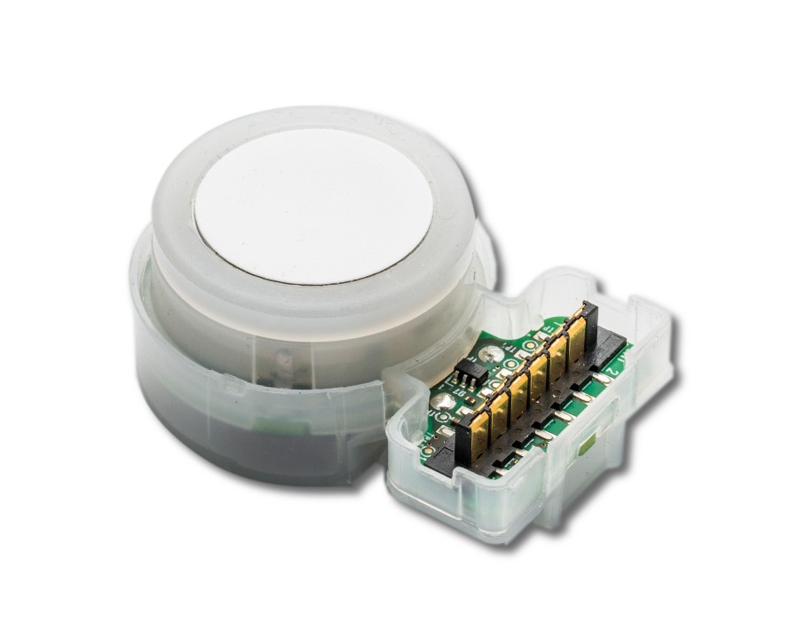 Round electronic sensor with a white top and exposed gold connector pins on a green circuit board.