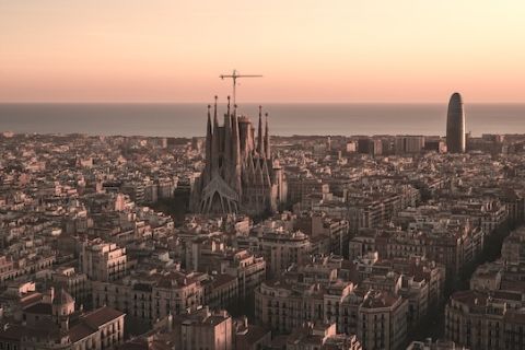 Aerial view of Barcelona city at sunset, featuring the Sagrada Família and the sea in the background.