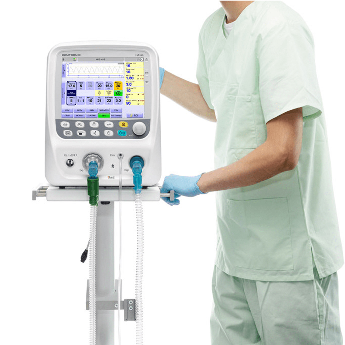 A healthcare worker adjusts a medical ventilator machine with a color display screen and tubes attached.