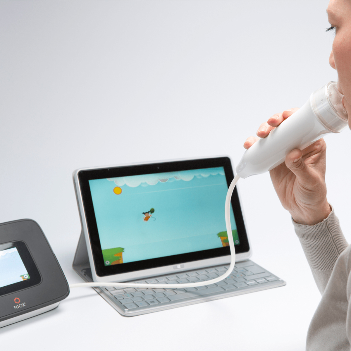 Person using a handheld spirometry device connected to a tablet, with a game displayed on the screen.
