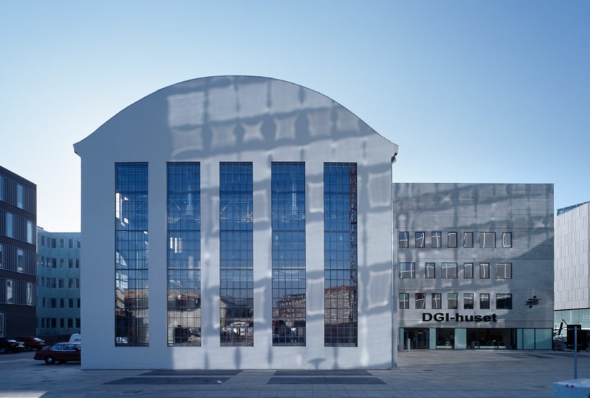 Modern building with tall arched windows and reflective glass, labeled "DGI-huset" on the front. Clear blue sky above.