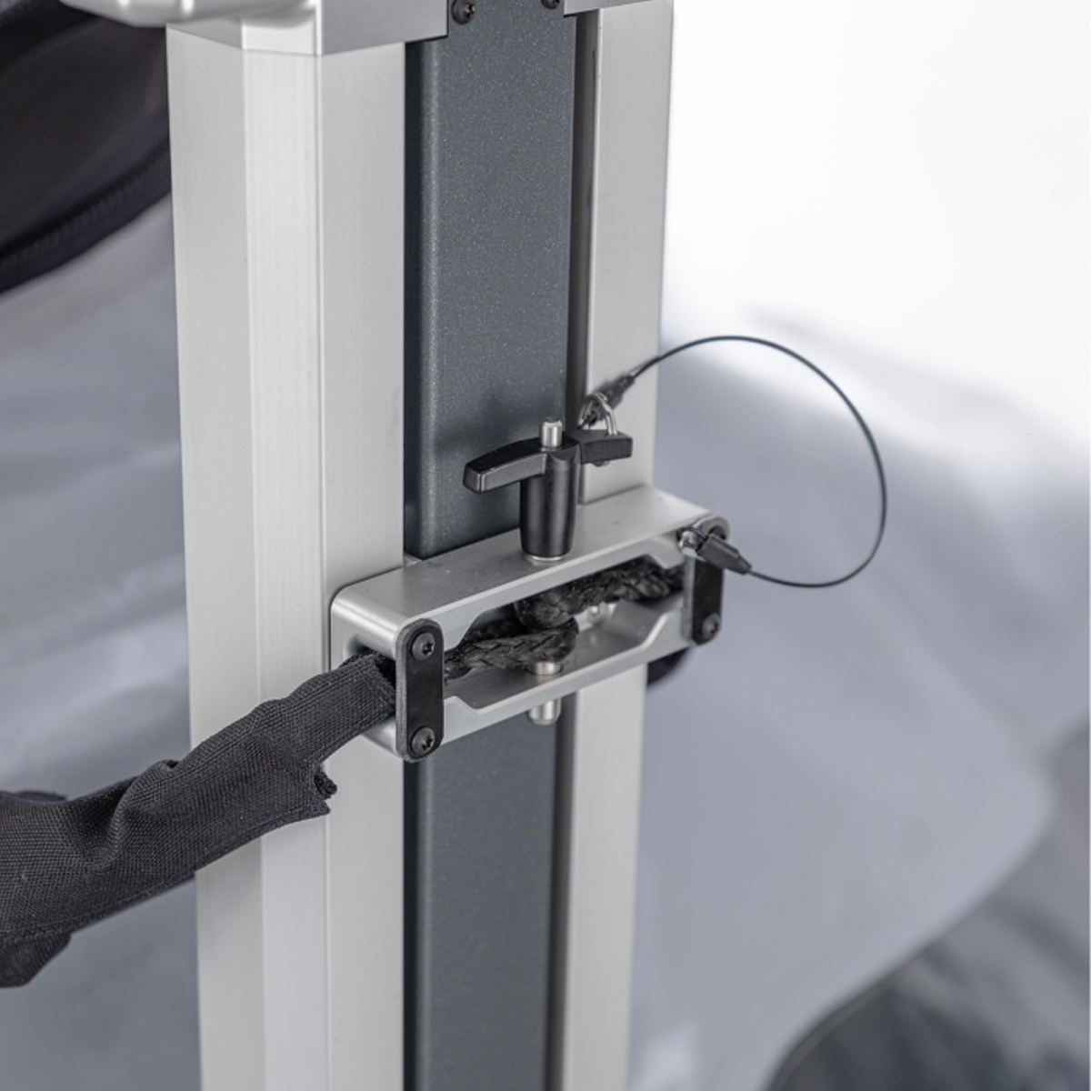 Close-up of a metal adjustable clamp bracket securing a fabric strap to an aluminum frame structure.