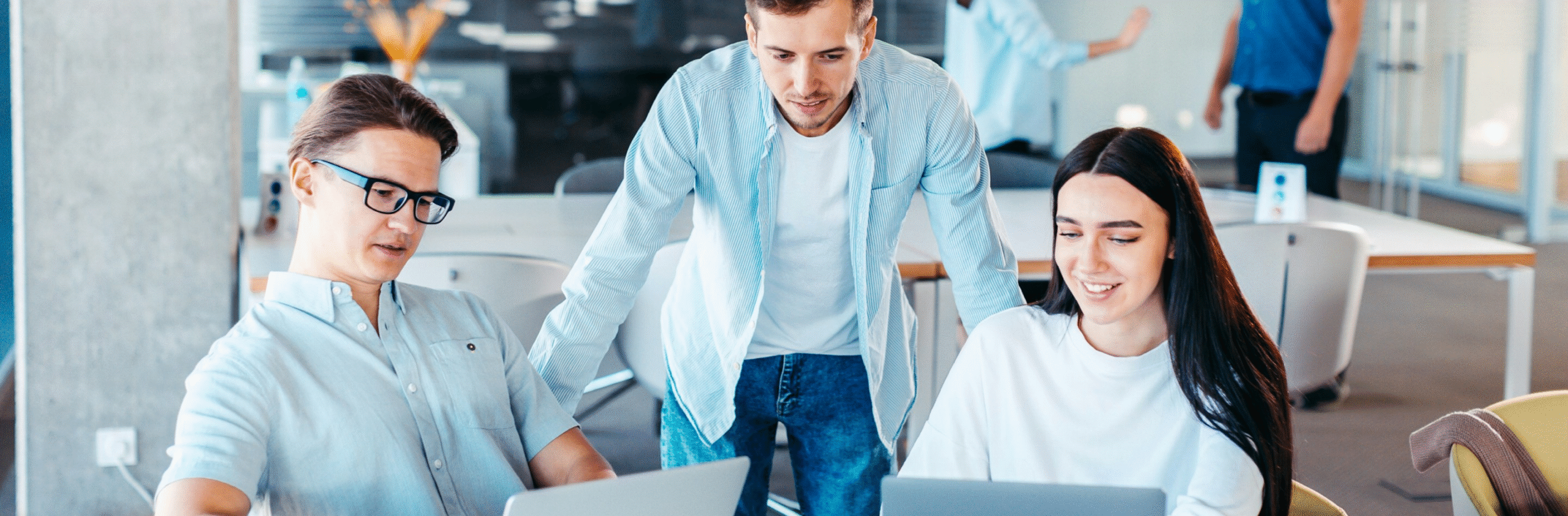 Three young professionals collaborating at laptops in a modern office space.