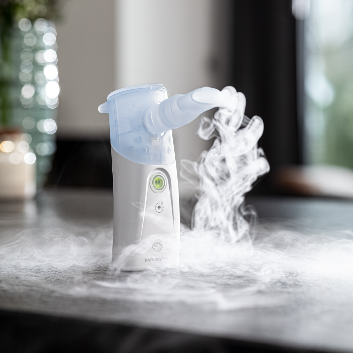 A medical nebulizer releasing visible mist, placed on a table in a well-lit indoor setting.